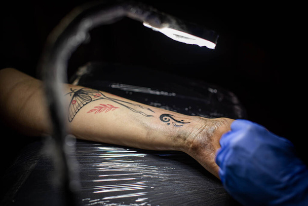 przycięty strzał procesu tatuażu na rękę w salonie. Profesjonalny tatuażysta wprowadza atrament do skóry używając igły z tatuaża.Profesjonalny tatuażysta pracujący w studio. - Zdjęcie, obraz
