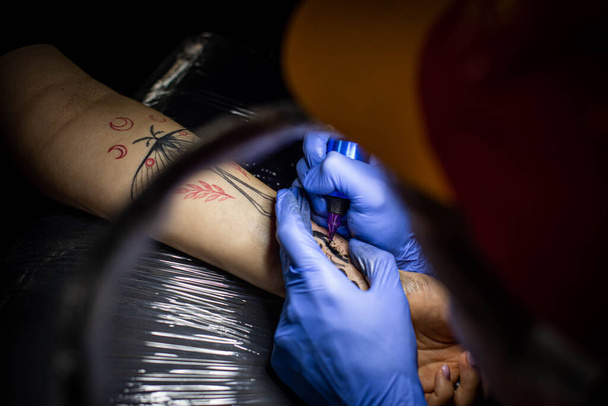 przycięty strzał procesu tatuażu na rękę w salonie. Profesjonalny tatuażysta wprowadza atrament do skóry używając igły z tatuaża.Profesjonalny tatuażysta pracujący w studio. - Zdjęcie, obraz