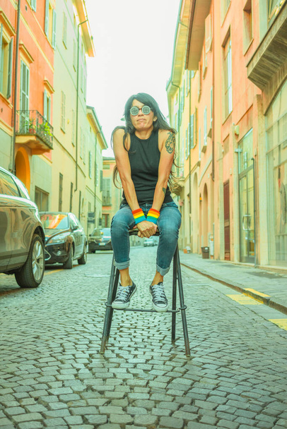 Atrakcyjna Latynoska kobieta w okularach przeciwsłonecznych siedząca na krześle na środku ulicy - Zdjęcie, obraz