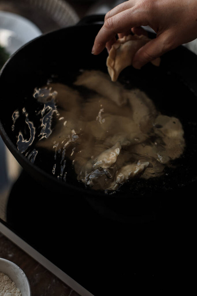 A hand putting a dumpling into a pan and waiting for the dumplings to be boiled in the kitchen - Fotó, kép
