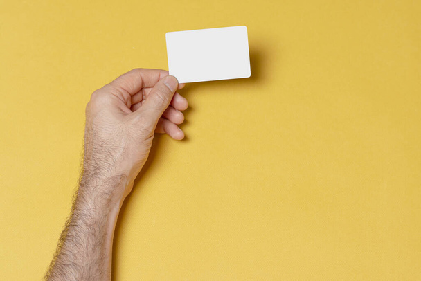 A male hand holding a blank business visit card against a yellow background - editable mockup template - Fotoğraf, Görsel