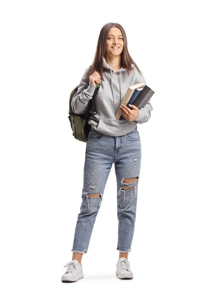 Full length portrait of a female student with a cap holding books and backpack isolated on white background - Zdjęcie, obraz