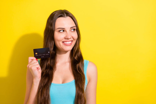 Photo portrait girl wearing blue singlet smiling showing bank card looking copyspace isolated vibrant yellow color background - Fotó, kép