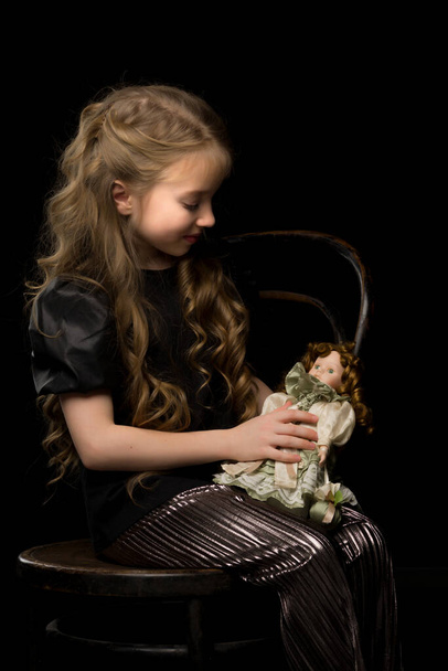 A little girl plays with a doll on a black background. - Fotoğraf, Görsel
