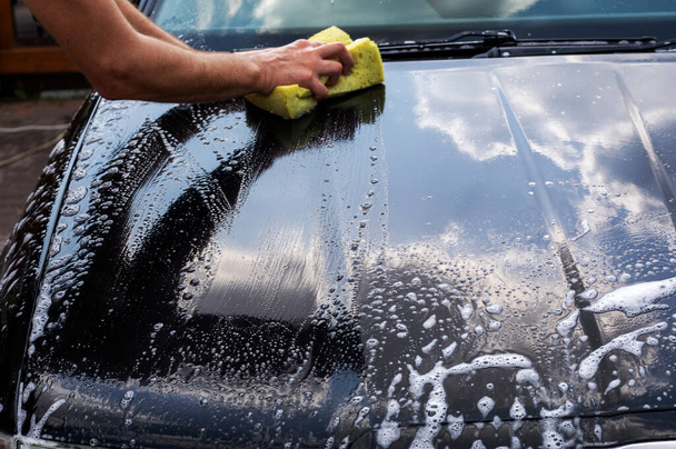 wash the hood of a black car on a sunny day in the garden after a flood, - Foto, Bild