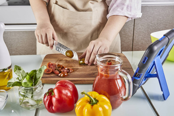 Teenager προετοιμάσει σπαγγέτι μπολονέζ από ένα online βιβλίο και ρολόγια ψηφιακή συνταγή στο tablet οθόνη αφής, ενώ την προετοιμασία υγιεινό γεύμα στην κουζίνα στο σπίτι. - Φωτογραφία, εικόνα
