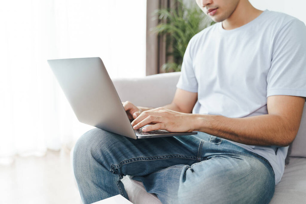 Hombre joven sentado en el sofá en casa escribiendo en el teclado del ordenador portátil para el trabajo en línea, el uso de Internet, freelancer, relajado, estilo de vida laboral moderno, el trabajo en casa - Foto, Imagen