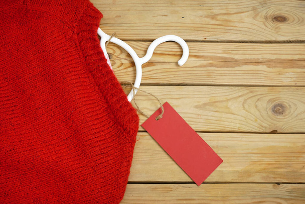 suéteres, bolsas en perchas sobre fondo de madera con etiqueta de precio rojo, concepto de consumo razonable, primer plano - Foto, imagen