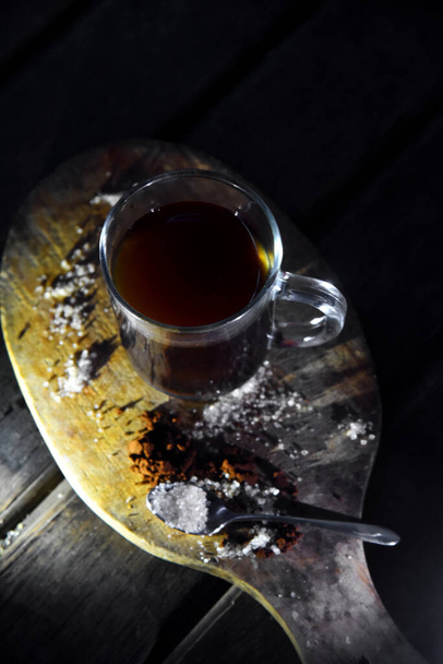 Etrafında şeker ve kahve tozu olan ahşap masanın üzerinde bir fincan kahve. - Fotoğraf, Görsel