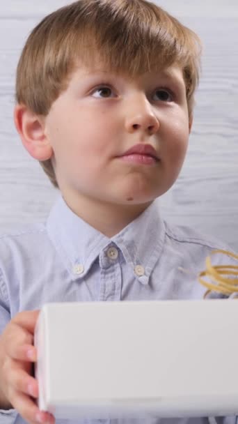 De jongen kreeg een doos met een geschenk dat hij bekijkt op een houten achtergrond.. - Video