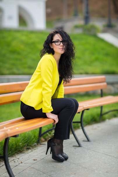 Beautiful girl is sitting on a park bench - Фото, зображення