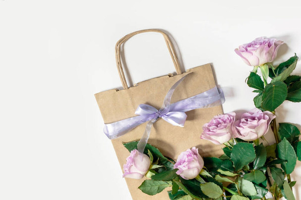 Bouquet from violet roses with shopping bag on the white background, top view, copy space. - 写真・画像