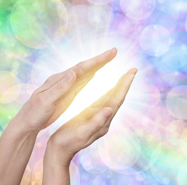 Scalar Healing Energy Field - Weibliche Hände, die sich gegen einen rotierenden, funkelnden Pfirsich und rosa Hintergrund mit Kopierraum in eine Kugel aus weißem Licht recken - Foto, Bild