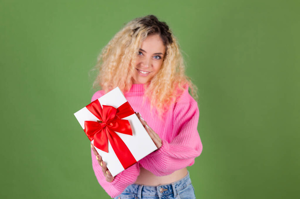 Fiatal szőke nő hosszú göndör haj rózsaszín pulóver zöld háttér ajándék doboz boldog vidám izgatott mosolygós - Fotó, kép