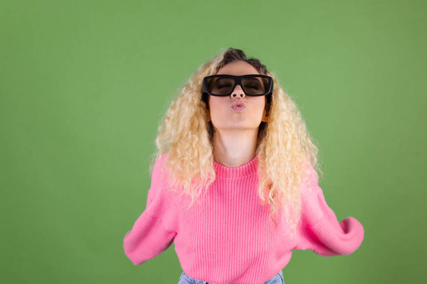 Young blonde woman with long curly hair in pink sweater on green background in 3d  cinema glasses playful smile  happy positive - Photo, Image