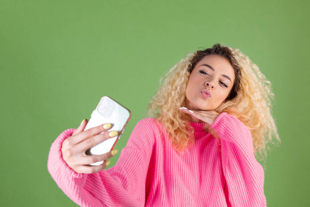 Woman in pink sweater on green background holding mobile phone posing take photo selfie - Fotó, kép