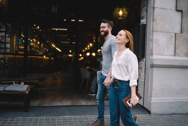 Happy delighted couple in casual wear being in wonderful mood and having great time together while enjoying romantic walk down city street holding hands - Foto, immagini