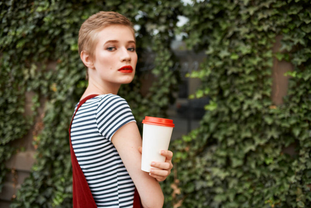 夏休みに茂みの近くの通りでコーヒーを手にした女性が - 写真・画像
