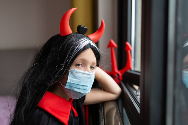 Portrait of cute Little Girl in costume of evil at home. Happy Halloween during coronavirus covid-19 pandemic quarantine concept. Kid wearing medical mask - Fotoğraf, Görsel