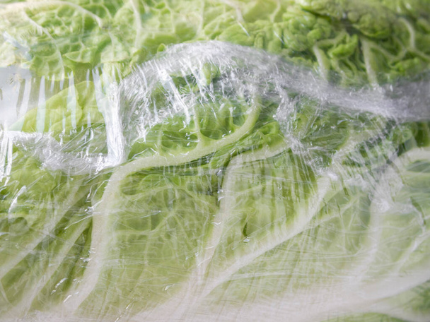Lettuce leaves wrapped in plastic wrap. - Фото, изображение