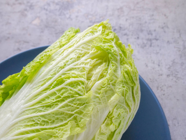 Top view of a piece of Chinese cabbage on a blue plate. Beautiful green leaves. - Фото, изображение
