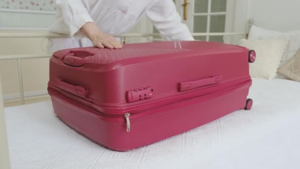 Nainen sulkee sängyllä suuri vaaleanpunainen matkalaukku vaatteet. - Materiaali, video