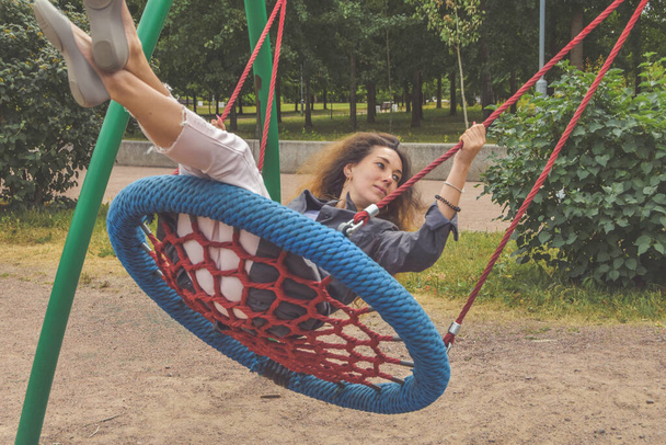 Ένα κορίτσι ταλαντεύεται σε μια κούνια στο πάρκο μια ηλιόλουστη μέρα - Φωτογραφία, εικόνα
