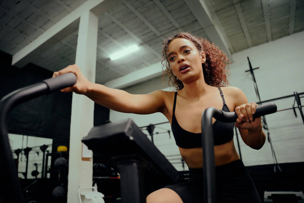 African American female using an elliptical trainer during cross training. Female athlete working out in the gym. High quality photo - Photo, image