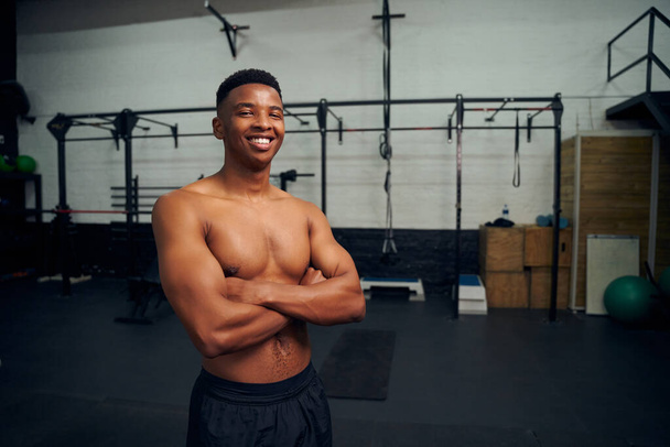 African American male standing with crossed arms and smiling to the camera. Male athlete looking happy while exercising in the gym. High quality photo  - Foto, imagen
