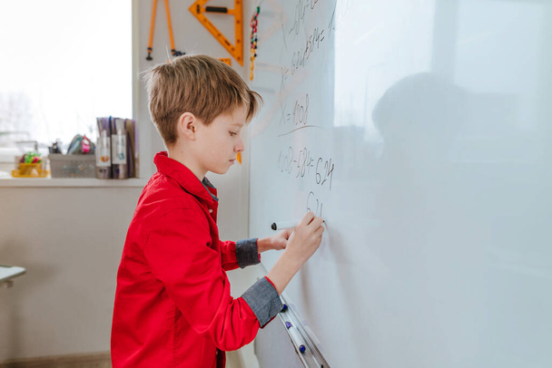 Μαθητής δημοτικού σχολείου γράφει στον πίνακα από τσόχινη άκρη στην τάξη - Φωτογραφία, εικόνα