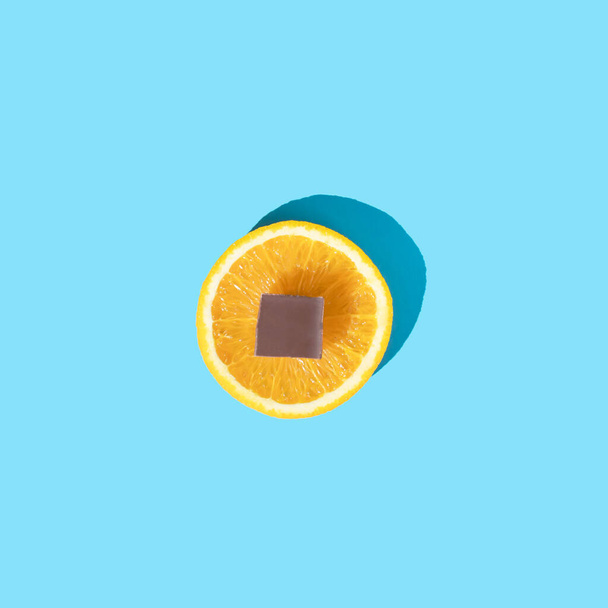 Orange mit Schokolade auf blauem Hintergrund. Minimales Sommerkonzept. Flach lag er. Ansicht von oben. - Foto, Bild