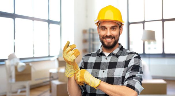 happy male builder in helmet and gloves at home - Zdjęcie, obraz