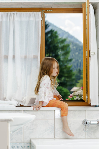 Cute little girl sitting on a bathroom window - Фото, изображение