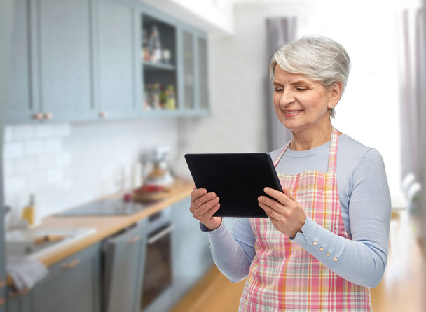 smiling senior woman in apron with tablet computer - Фото, зображення