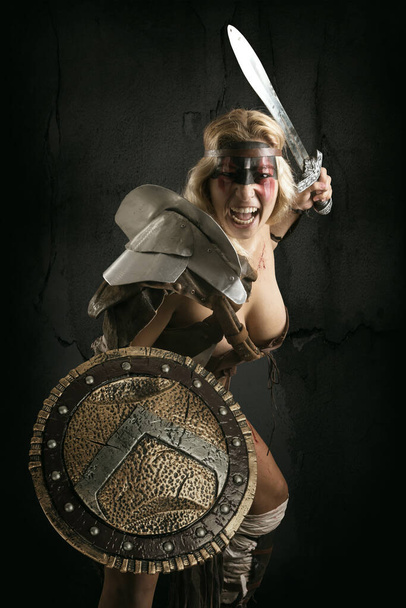Древняя женщина воин или Гладиатор позирует с мечом и щитом, изолированные в темном фоне - Фото, изображение