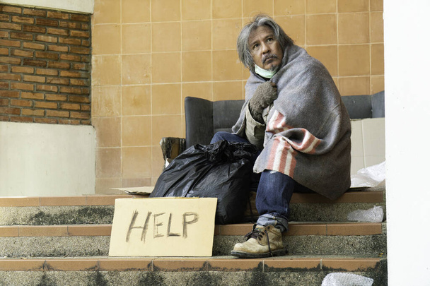 ホームレスの男が通りに座っている。大都市の問題. - 写真・画像