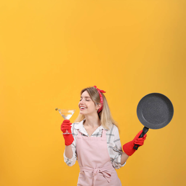 Young housewife with frying pan and glass of martini on yellow background - Photo, Image