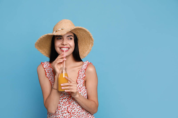 Beautiful young woman with straw hat and bottle of refreshing drink on light blue background. Space for text - Φωτογραφία, εικόνα