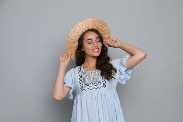 Beautiful young woman with straw hat on light grey background - Foto, afbeelding