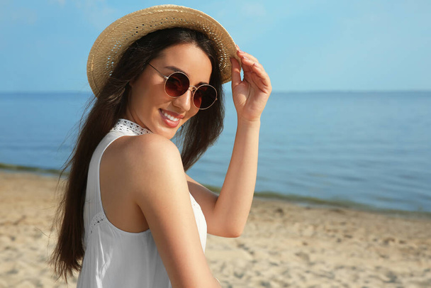 Beautiful young woman with straw hat and sunglasses on beach. Stylish headdress - Zdjęcie, obraz