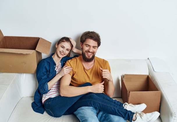 мужчина и женщина сидят на диване и двигают коробки с вещами семейного новоселья - Фото, изображение
