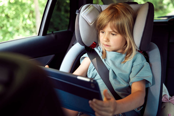 Маленька дівчинка на задньому сидінні автомобіля з планшетом
 - Фото, зображення