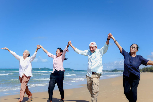 Grupo de cuatro viejos amigos ancianos alegres viajan al aire libre juntos, sosteniendo y levantando las manos mientras corren en la playa, se divierten y disfrutan de pasar tiempo, descansando y relajándose en vacaciones.  - Foto, imagen