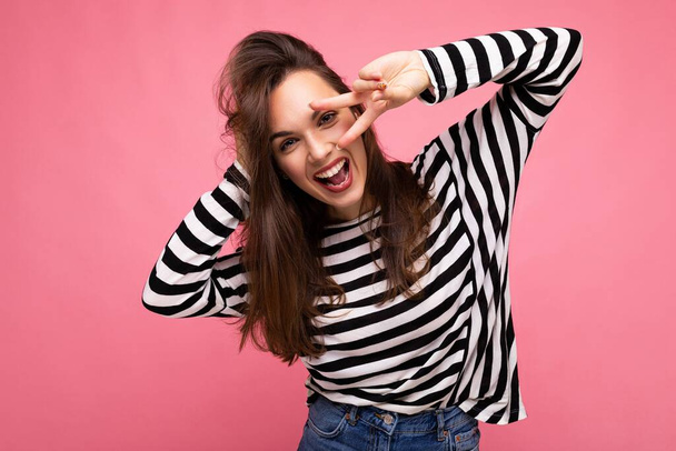 Photo of young european positive smiling winsome joyful happy beautiful brunette woman with sincere emotions wearing casual striped pullover isolated on pink background with copy space - Photo, Image