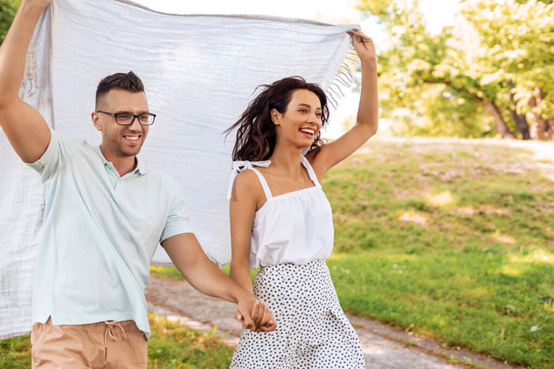 happy couple with picnic blanket at summer park - Fotoğraf, Görsel