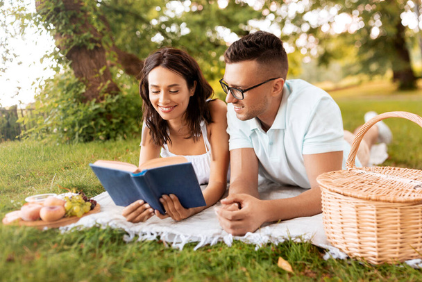 happy couple reading book on picnic at summer park - Fotó, kép