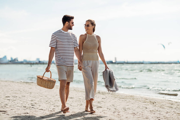happy couple with picnic basket walking on beach - Фото, изображение