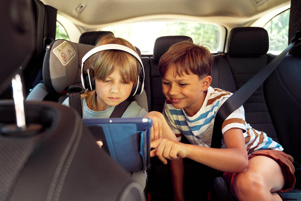 Szczęśliwe rodzeństwo na tylnym siedzeniu samochodu z tabletem - Zdjęcie, obraz