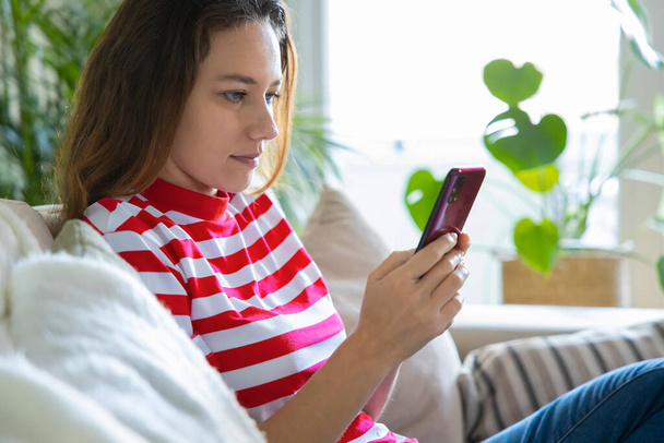Young woman using mobile phone while sitting a sofa at home  - Photo, Image