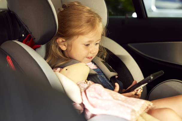 Cute little girl sitting in the baby car seat with phone - Fotó, kép